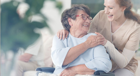 Seated older woman with a carer beside her putting a hand on her shoulder